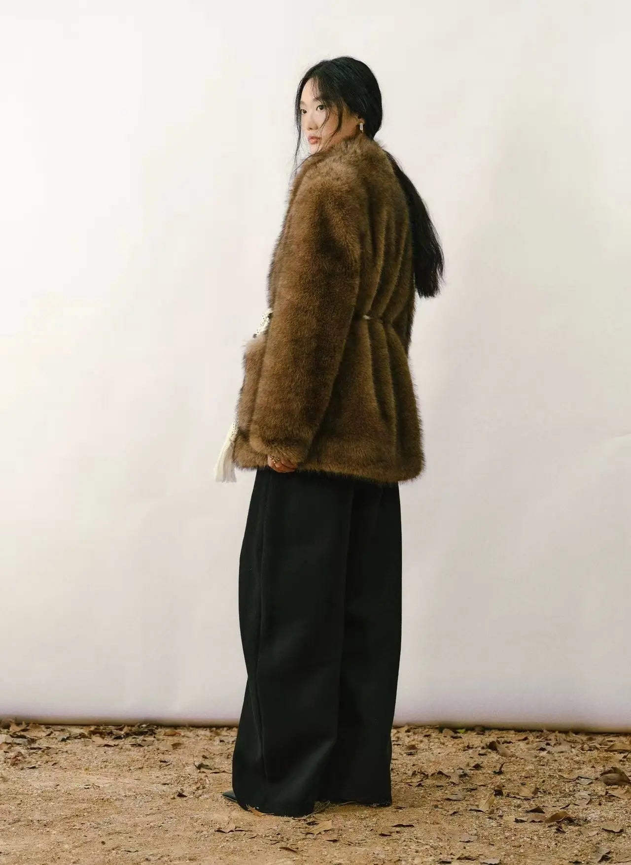 Woman wearing a black faux fur coat over an evening gown in a brightly lit city setting.